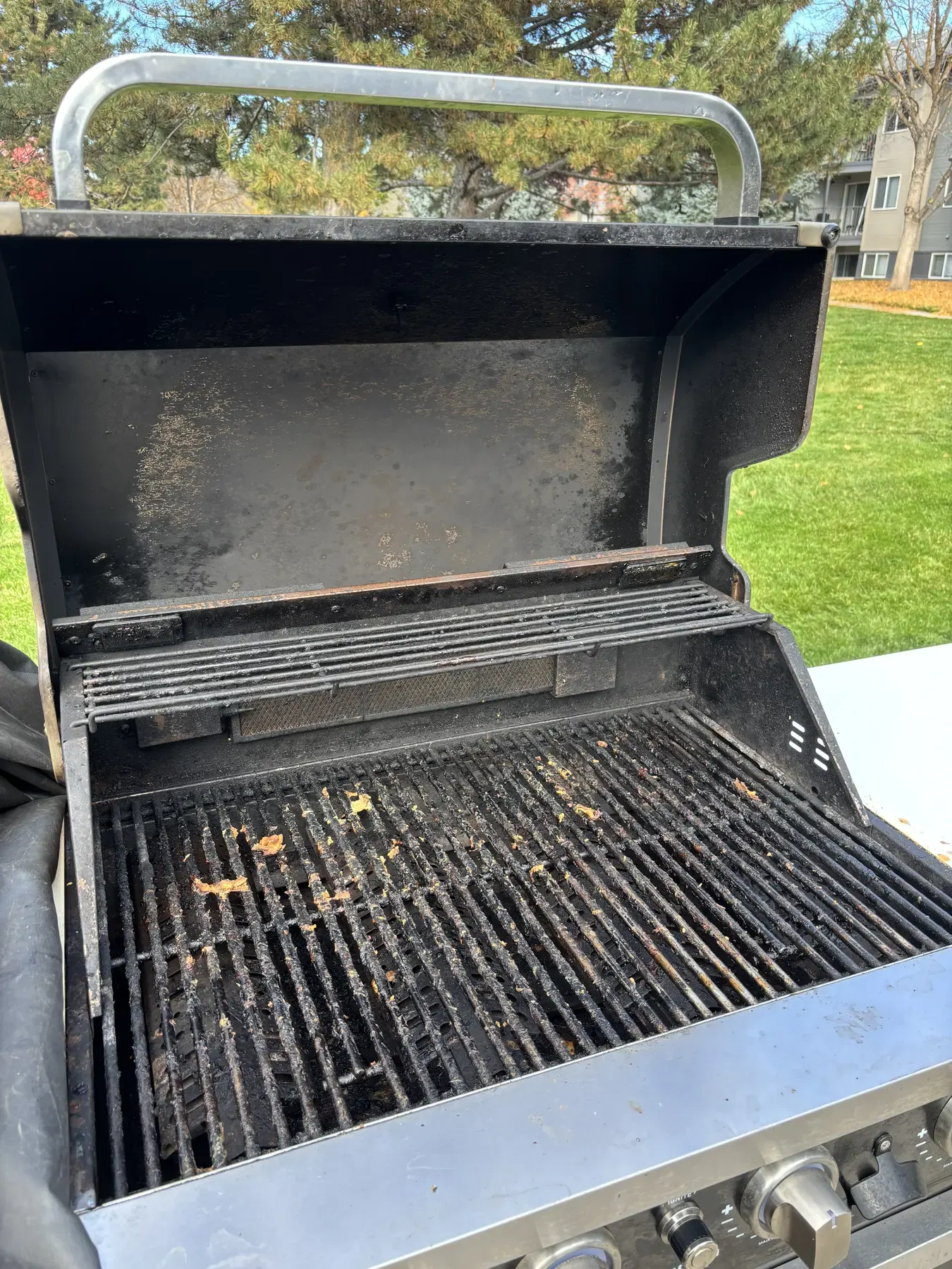 An open gas grill with grease and food debris caked on the cooking grates, warming rack and inside of the lid.