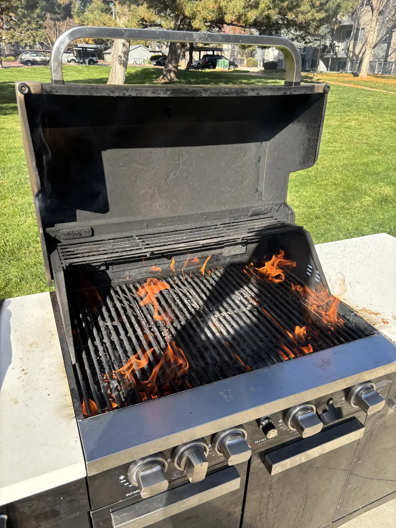 An open gas grill with flames rising up through greasy cooking grates.